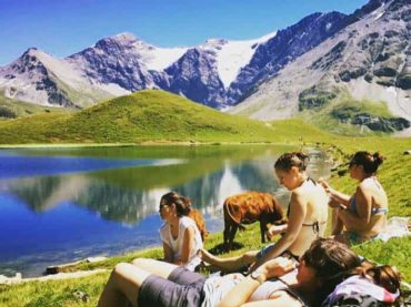 People sitting by glacial lake wit the cows