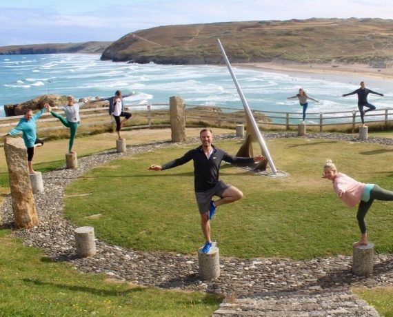 people standing on stones doing yoga pose on cliff next to sea easter yoga retreat cornwall