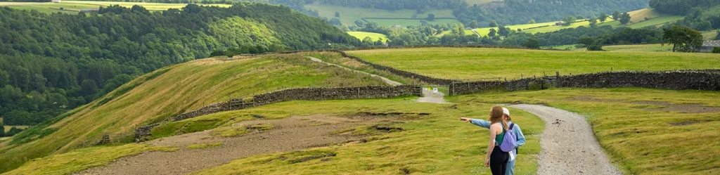 trail going down the rolling hills in the peak district with a person pointing to the views